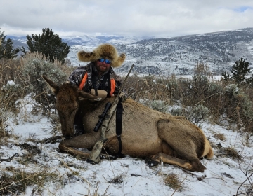 A happy hunter posing in his fur hat with his cow elk and rifle